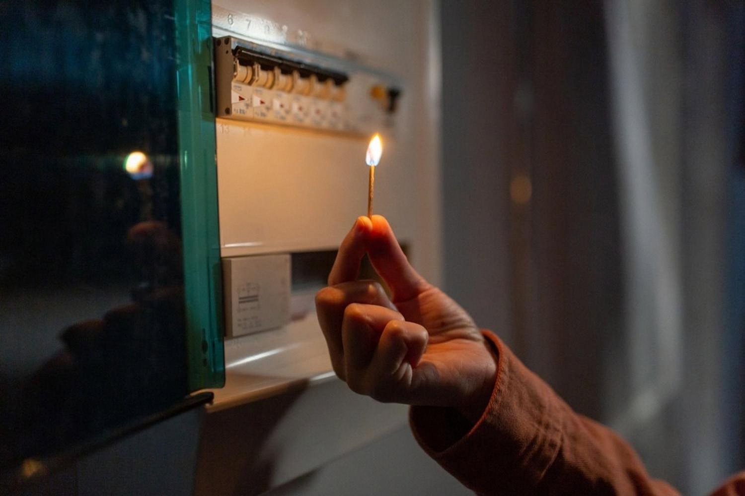 Person holding a lit match near a dark fuse box during a home power outage