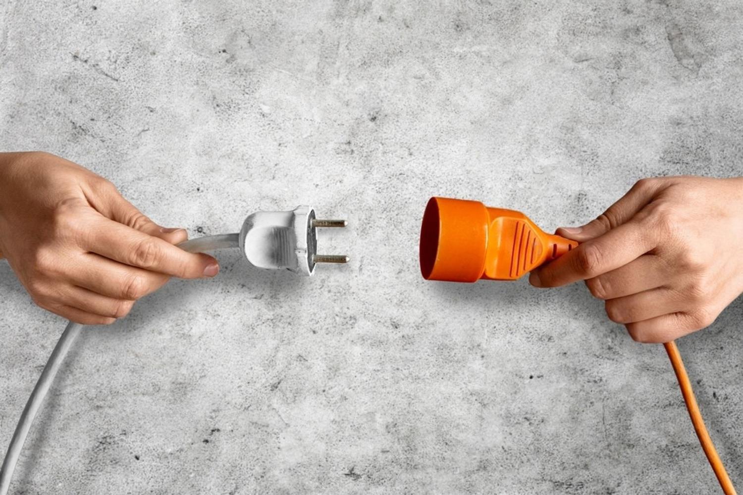 Two hands pulling apart a plug and socket to safely disconnect an electrical cord